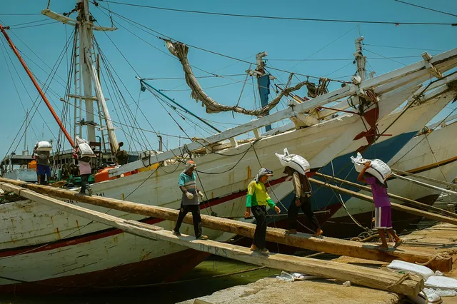 Wooden pinisi boats moored at a jetty, crew crossing the gangplanks between hulls