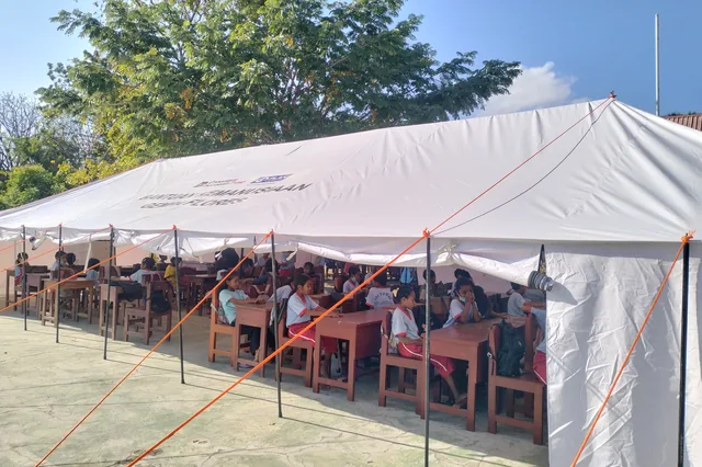 Primary school children at wooden desks under an emergency tent marked Humanitarian Aid, Flores Earthquake