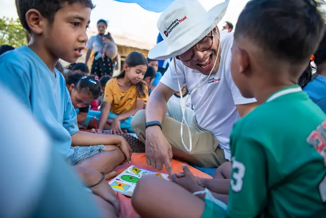 A volunteer plays a learning card game with two boys at the NTT post