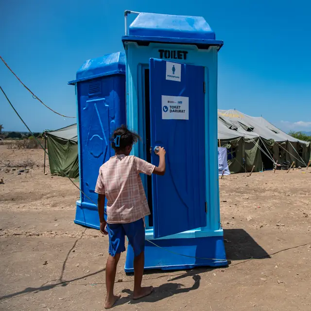 A child opens the door of an emergency aid toilet at the camp