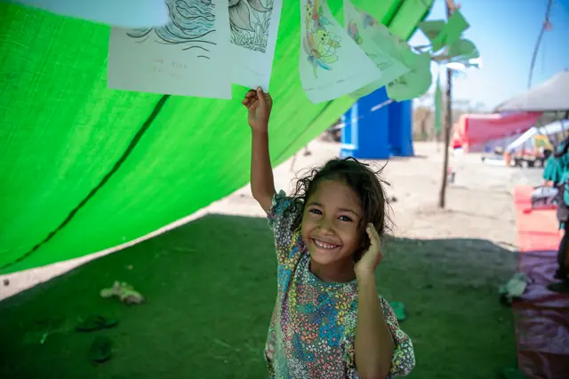 A girl smiles as she holds up her drawing in the learning tent