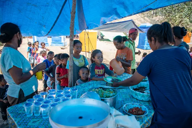 Volunteers serve food and drinks to children at a communal kitchen in the NTT camp