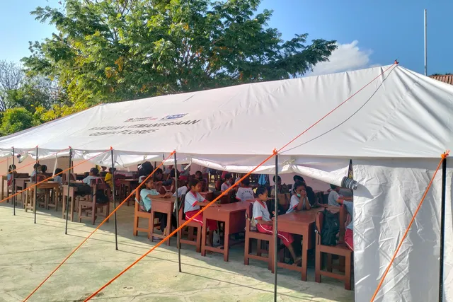 SDI Towak pupils study beneath an emergency classroom tent marked Flores Earthquake Humanitarian Aid